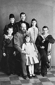 Black-and-white photograph of bald and bearded Alexander III wearing a military uniform and surrounded by his children and wife.