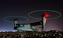 Ground crew refuel an MV-22 before a mission in central Iraq at night. The rotors are turning and the tips are green, forming green circles.