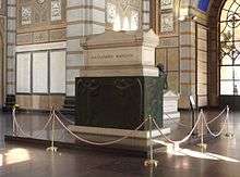 A white marble sarcophagus elevated on a black pedestal, inside a chapel