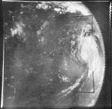 Grayscale image of a tropical cyclone as viewed from space. Due to the position of the camera, the tropical cyclone is at center-right, with banding features visible. As a result of the camera angle, the limb of the Earth is clearly visible; outer space appears a uniform dark gray.