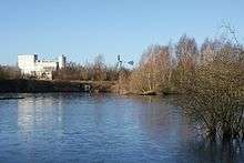 Large pool with scrub on the right and a large white industrial building in the background