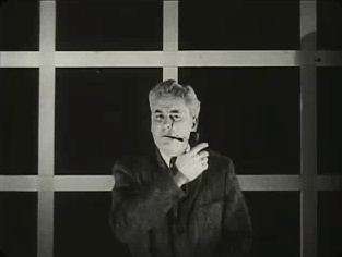 Black and white portrait of Dr. Ivey wearing a dark suit and tie-with a white shirt. He is holding the end of his trademark pipe with one hand held up and across his chest with the pipe in a smoking position up to his mouth pointing out in the same direction. The background looks white with squares cut out showing black behind, like the pattern of small windows in some glass doors.