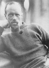 Head and upper body of a seated man, balding, smoking a pipe. He is wearing a heavy jersey.