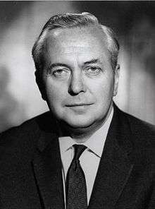 Grey-scale portrait of a middle-aged man with a round face and coiffed grey hair, wearing a dark suit