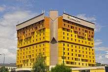 A 12-story hotel building with a yellow- and brown-coloured exterior. Trees are visible in the foreground, and the building reads "Holiday Inn" at the top.