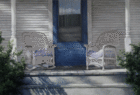 gorgeous oil painting, close-up of white house porch with blue door, wicker chair and rocking chair,both empty; with steps in front and dark green bushes to sides