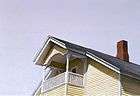 oil painting of partial upward view of balcony of yellow house with red chimney and pale blue sky