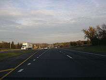 Eastbound IL 120 west of Hunt Club Road. Road is divided highway with a grassy median and open areas on both sides with scattered trees.