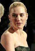 A young woman with blonde hair wears earrings and a black strapless dress.