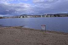 A metal sign erected on the sandy shores of the lake advises of the ban on water activity due to pollution