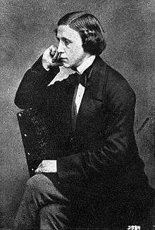 tinted monochrome 3/4-length photo portrait of seated Dodgson holding a book