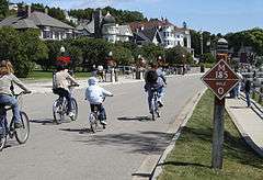Bicyclists on a road. Houses can be seen at left.