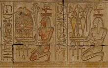 Relief showing two kneeling people carrying trays piled with plants, jars of liquid, and food.