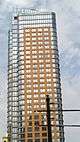 Oro, a high-rise clad in stone and blue glass with curved corners, viewed on the left from street level