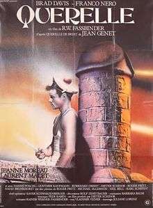 A man in a sailor uniform leads with his back on a large brick phallus sculpture.