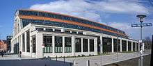 A long, large building with a barrel-vault roof rising above a facade with full-length plate-glass windows along the length of the building