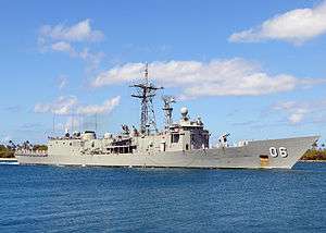 A grey warship sailing near the shoreline.